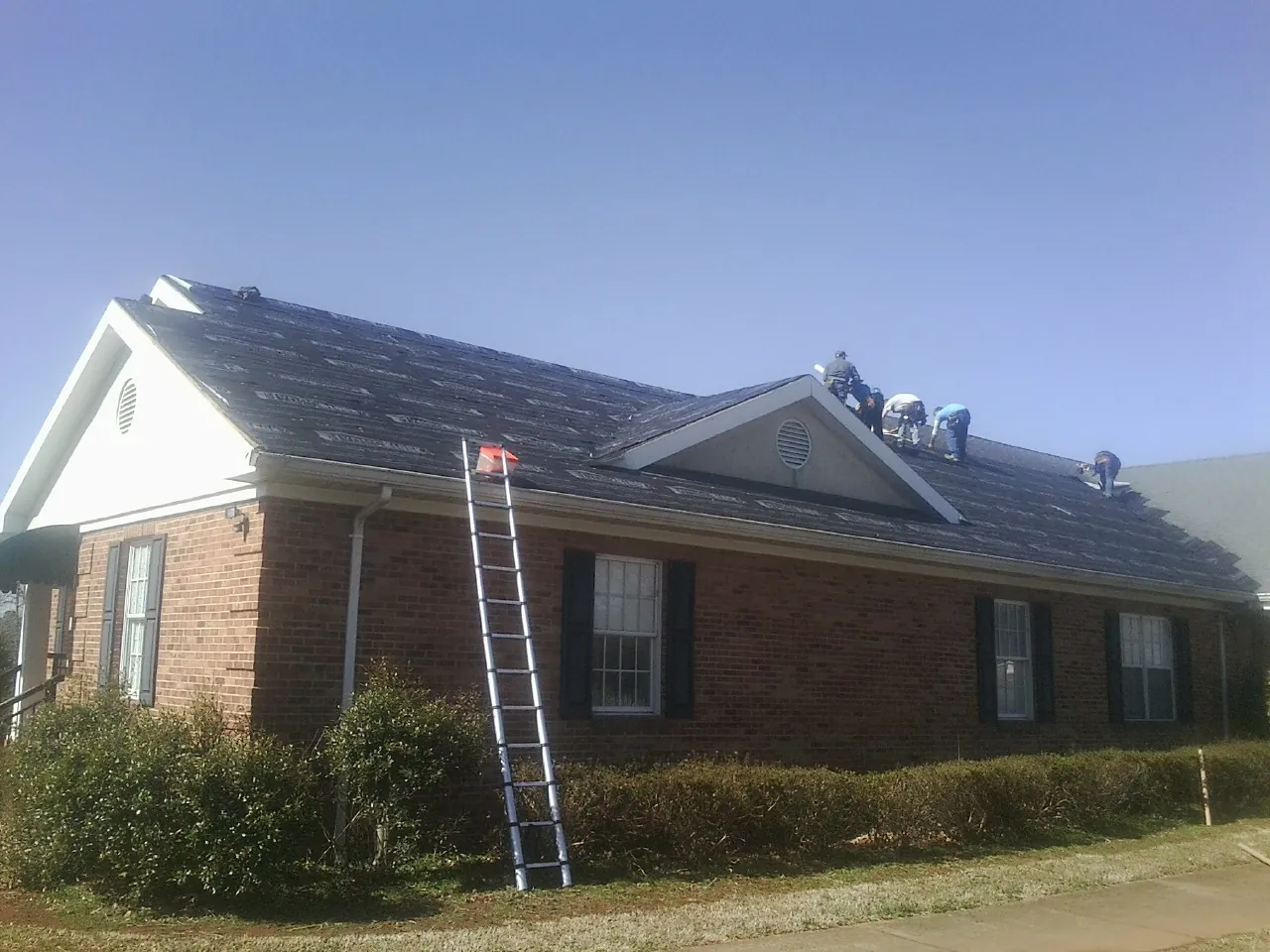Crew tearing shingles off a brick ranch roof with a ladder set — Metal Roof Repair work by our crew in Buckingham