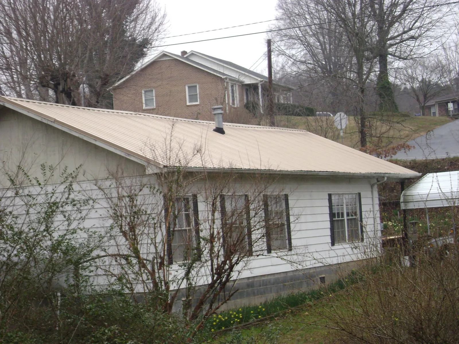 Tan metal roof on a white sided house set into a hillside — Commercial Roofing by Roofing Brothers in Buckingham